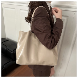 Detail of beige faux leather tote bag with chain strap shown on a model's shoulder