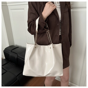 Detail of white glossy patent leather tote bag with elegant gold chain shoulder strap