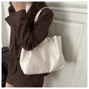 Detail of white glossy leather tote bag featuring gold chain strap and side stud rivets