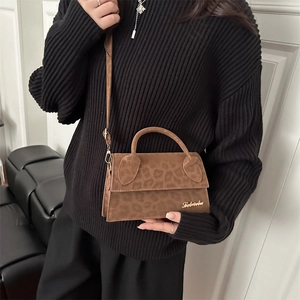 Petit sac bandoulière léopard marron en daim avec logo doré porté sur un pull noir