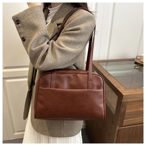Close-up of a dark brown leather Boston bag with a sleek front pocket on a model