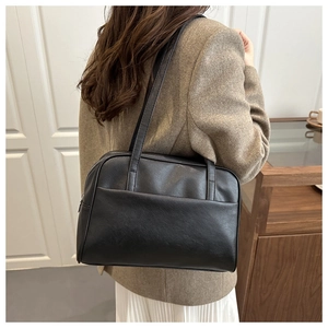 Detail of minimalist black leather tote bag with slim straps worn on female shoulder