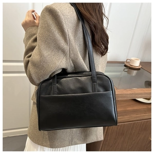 Close-up of a black leather tote bag with side pocket shown on a model's shoulder
