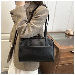 Minimalist black faux leather tote bag with front pocket shown on a shoulder in a casual look
