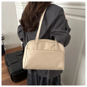 Close-up of a beige faux leather tote bag worn by a model in a grey blazer jacket