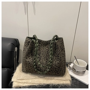 Detalle de bolso leopardo con asas trenzadas verde oliva sobre un chal de flecos suave