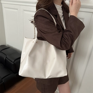 Chic off-white patent leather tote bag with chain strap shown on model in modern room