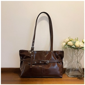 Gros plan sur un sac cabas marron foncé brillant avec boucle de ceinture et œillets en métal