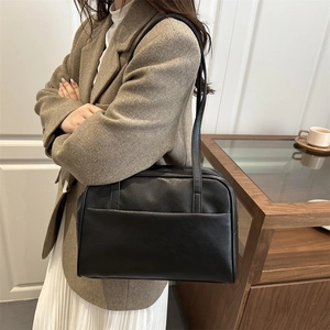 Minimalist black faux leather tote bag with shoulder strap shown in a stylish lifestyle setting
