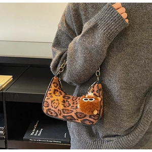 Chic leopard print crescent bag with plush charm and golden chain detail worn by a model