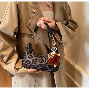 Close-up of leopard print baguette bag with plush monster charm and gold chain strap
