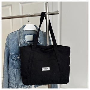 Detail of black corduroy tote bag with Fashion Instinct label hanging on metal rack