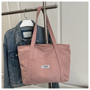Detailed texture of pink corduroy tote bag with white woven label on a denim jacket background