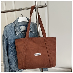 Detail of dark brown corduroy tote bag with fashion instinct patch and textured material