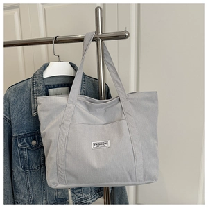 Detail of grey corduroy tote bag featuring an embroidered Fashion Instinct patch and front pocket