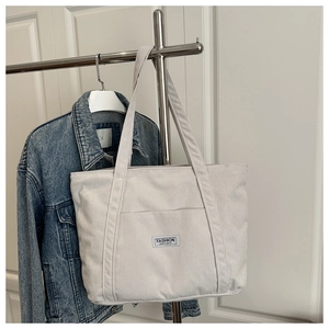 Detailed view of light grey corduroy tote bag featuring a front pocket and textile label
