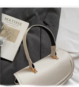 Detail of minimalist beige handbag showing gold metal hardware and stitched handle