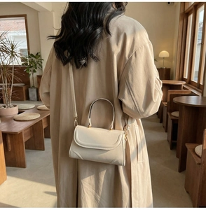Detail der cremefarbenen Ledertasche mit goldener Hardware und gebogenem Handgriff