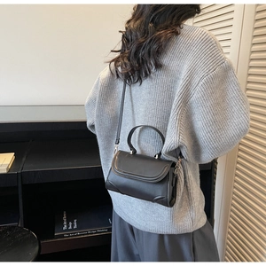 Detailed view of a black leather rectangular handbag with round handle and slim strap