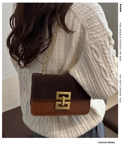 Detail der zweifarbigen Kettentasche mit goldener Schnalle auf beigem Pullover