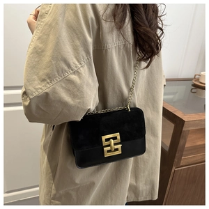 Detail of black crossbody bag featuring gold chain and square metal clasp on a coat