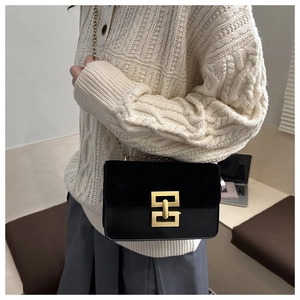 Close-up of black leather crossbody bag with gold geometric buckle and chain strap