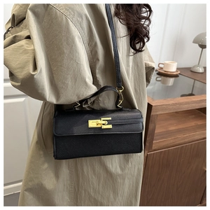 Détail du sac carré en cuir noir avec boucle dorée et bandoulière sur une femme