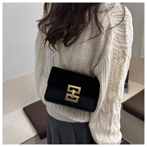 Detail of black leather crossbody bag with gold chain strap and square metal lock clasp