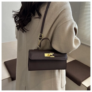 Détail du mini sac Kelly en cuir marron foncé avec boucle dorée sur un manteau en laine