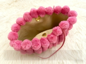 Detail of pink plush tote bag showing magnetic snap closures and furry pom-pom edges