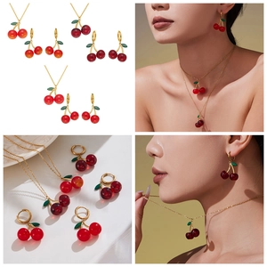 Detail of red cherry pendant necklace and earrings with gold chains on a model