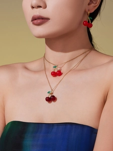 Detailed view of layered cherry necklaces and matching earrings on a female model