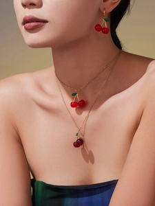 Close-up of red cherry jewelry set including hook earrings and layered gold necklace