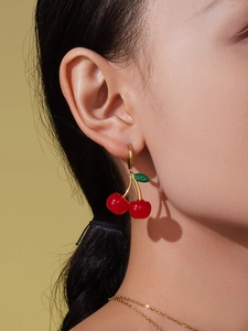 Close-up of translucent red cherry earrings with green leaves on gold hooks for women