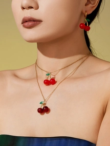 Detail of red cherry pendant jewelry set with golden chain on model on yellow background