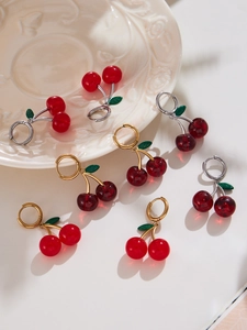 Close-up of cherry fruit earrings with green leaves on white plate background