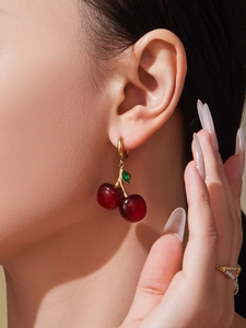 Detailed view of red resin cherry earrings with golden hooks on a fashion model