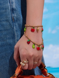 Detail of fruit charms on gold bracelets and leaf rings worn in an outdoor setting