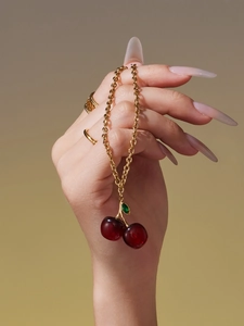 Detail shot of a red resin cherry pendant with gold leaf and matching gold necklaces