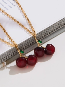Close-up of red resin cherry pendant necklaces with gold chains on magazine page