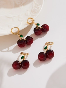 Detail of cherry earrings with red resin fruit, gold branch, and green leaf accents