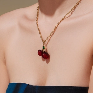 Red resin cherry pendant necklace with gold metal chain and green leaf on model