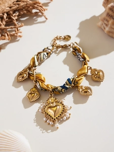 Dettaglio di ciondoli a cuore dorati bohémien e tessuto di seta su un bracciale vintage
