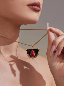 Vue rapprochée du pendentif géométrique en émail noir et pierre rouge sur chaîne dorée