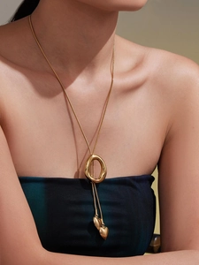 Close-up of a gold lariat necklace with irregular metal ring and heart pendants