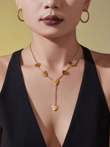 Close-up of golden heart pendant Y-necklace and twisted hoop earrings on a model