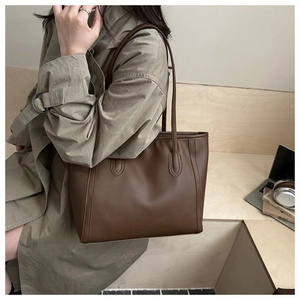 Détail d'un grand sac cabas en similicuir marron foncé porté avec un trench élégant