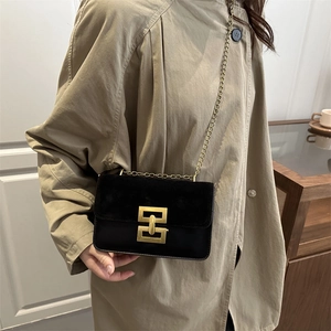 Schwarze Umhängetasche mit goldener Schließe und Kette auf einem beigen Mantel
