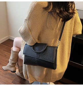 Chic black crossbody bag featuring snakeskin texture and round metal handle detail