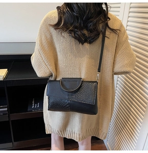 Détail d'un sac bandoulière noir effet serpent porté avec un pull beige en maille
